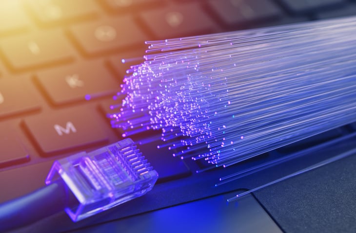 Fiber optics in blue, close up with ethernet and keyboard background, warm lens flare