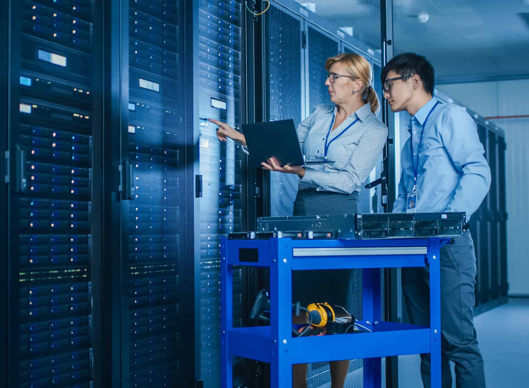 In the Modern Data Center: Engineer and IT Specialist Work with Server Racks, on a Pushcart Equipment for Installing New Hardware. Specialists Doing Maintenance and Diagnostics of the Database.